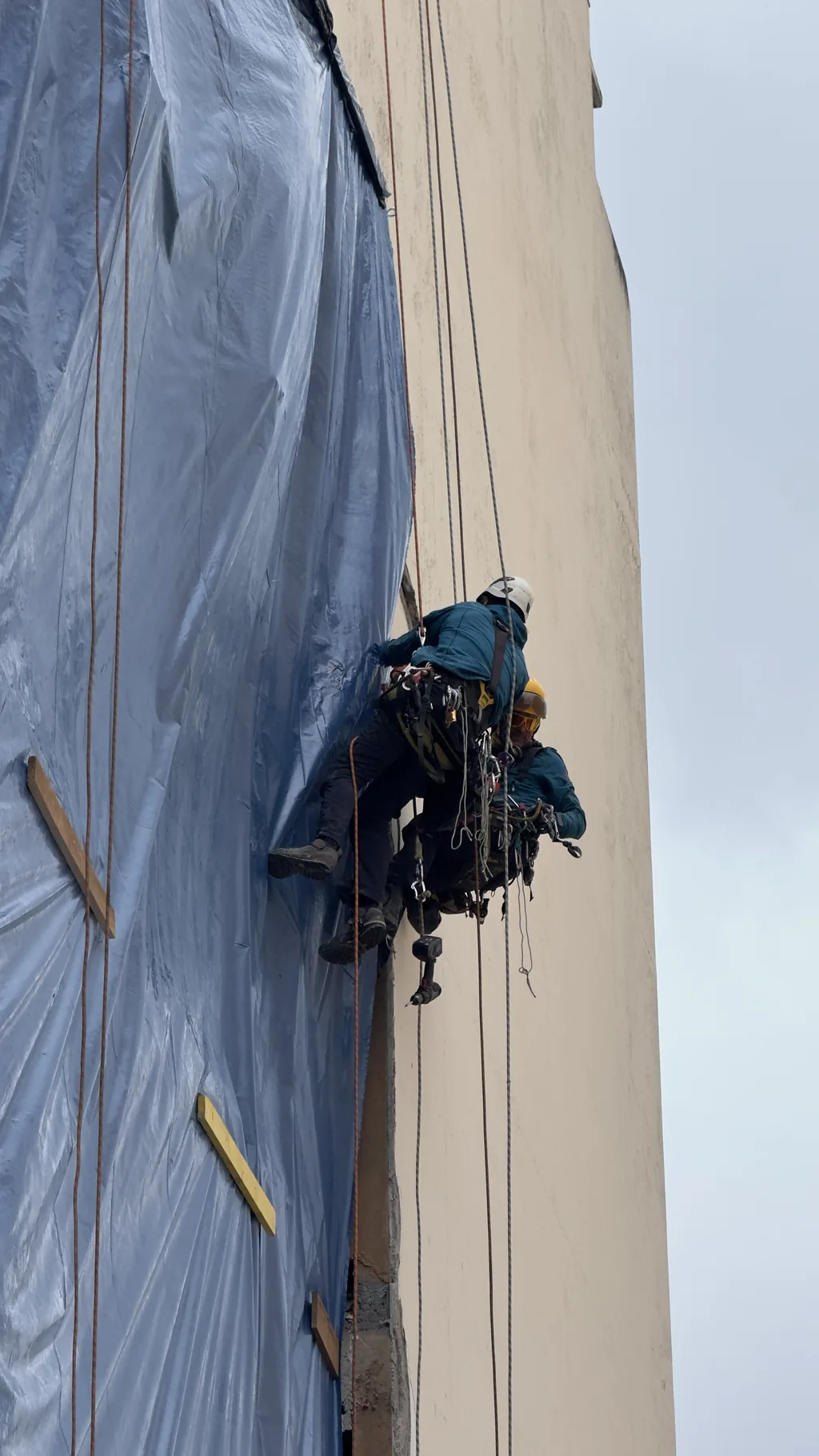 Rope access technician on a facade protected by a tarpaulin