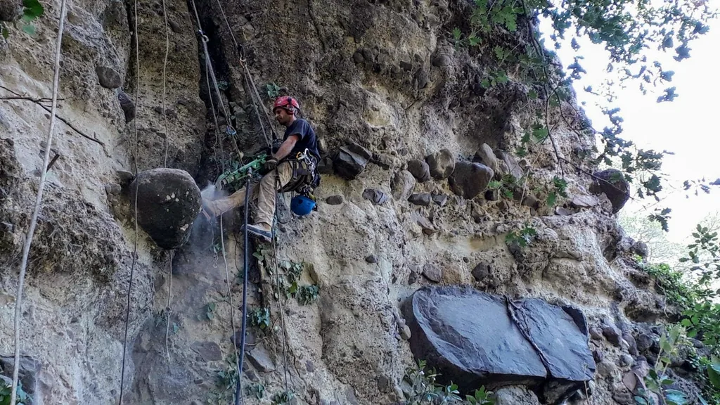 Rope access technician drilling next to a boulder