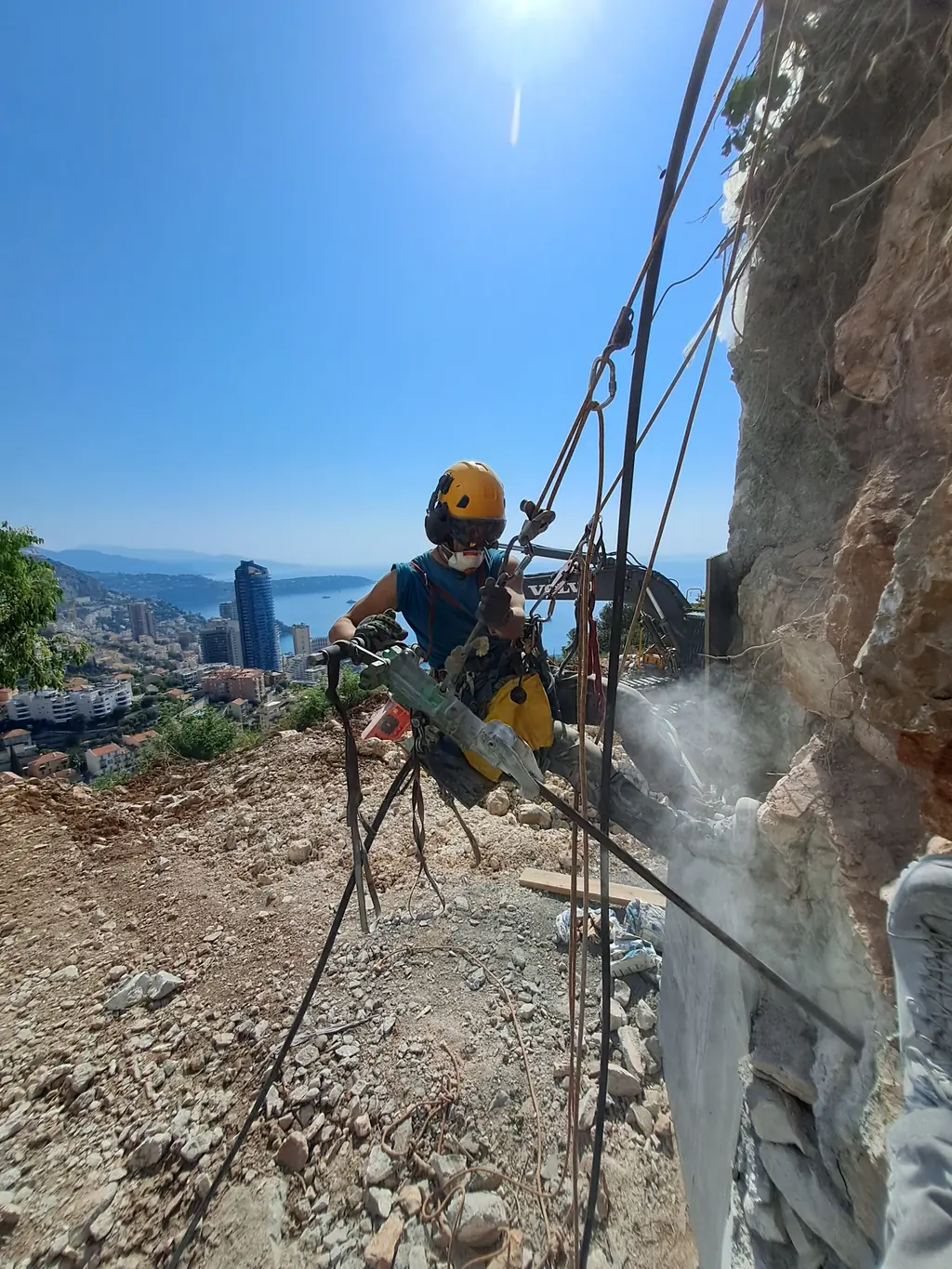 Rope access technician with a rotary hammer on a rock face