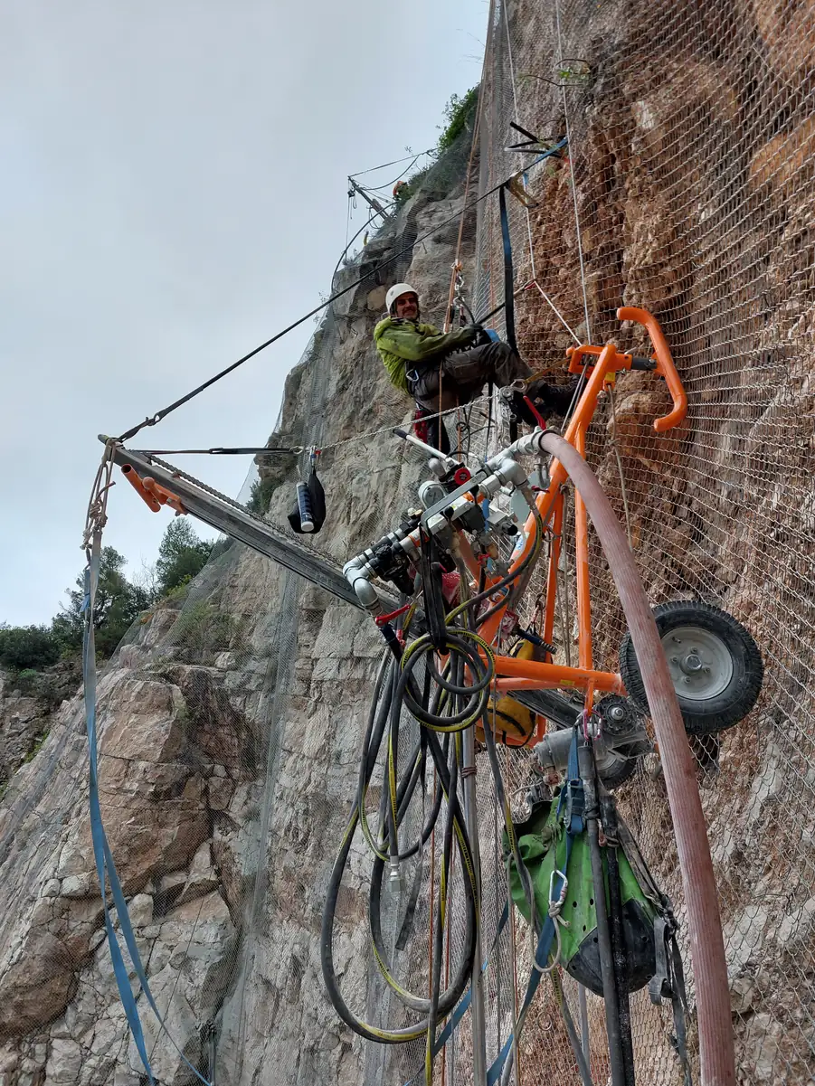 Rope access technician and drilling rig on a meshed rock face