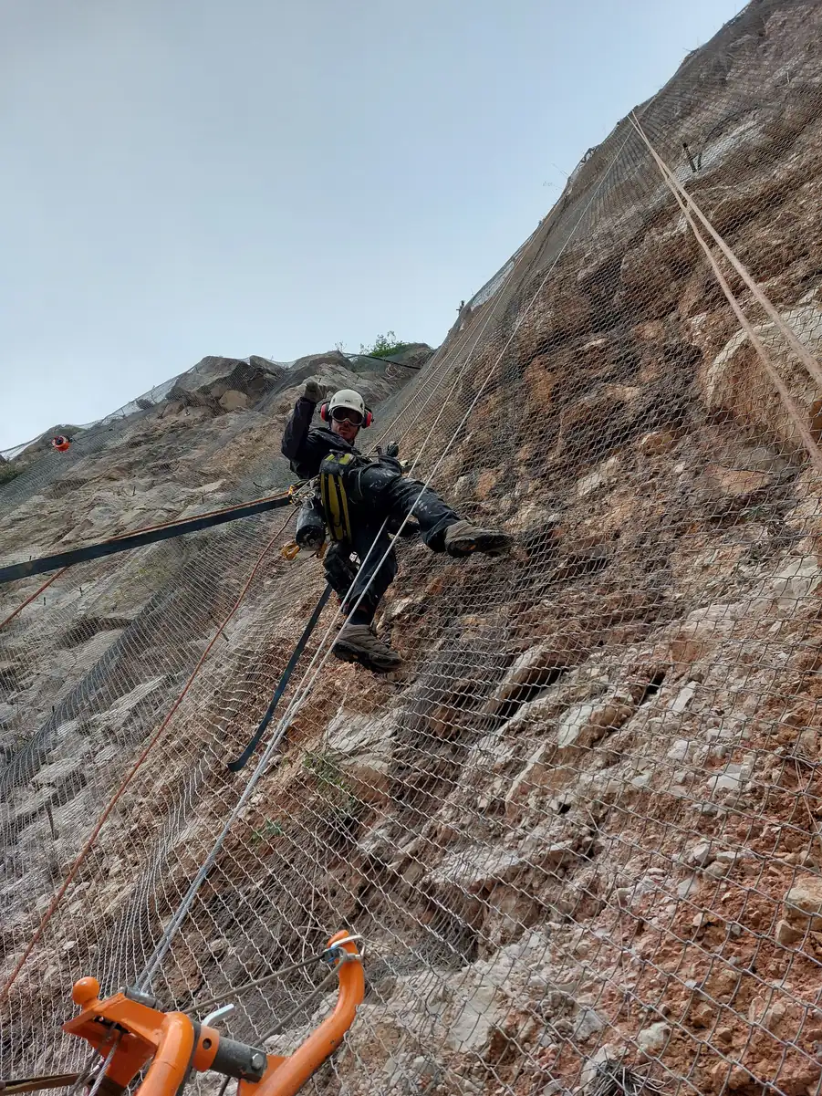 Rope access technician working on a rock face protected by mesh