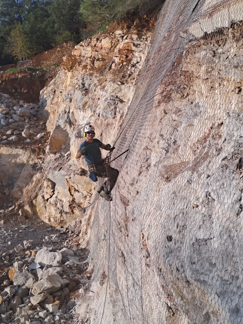 Rope access technician on a rocky embankment being meshed