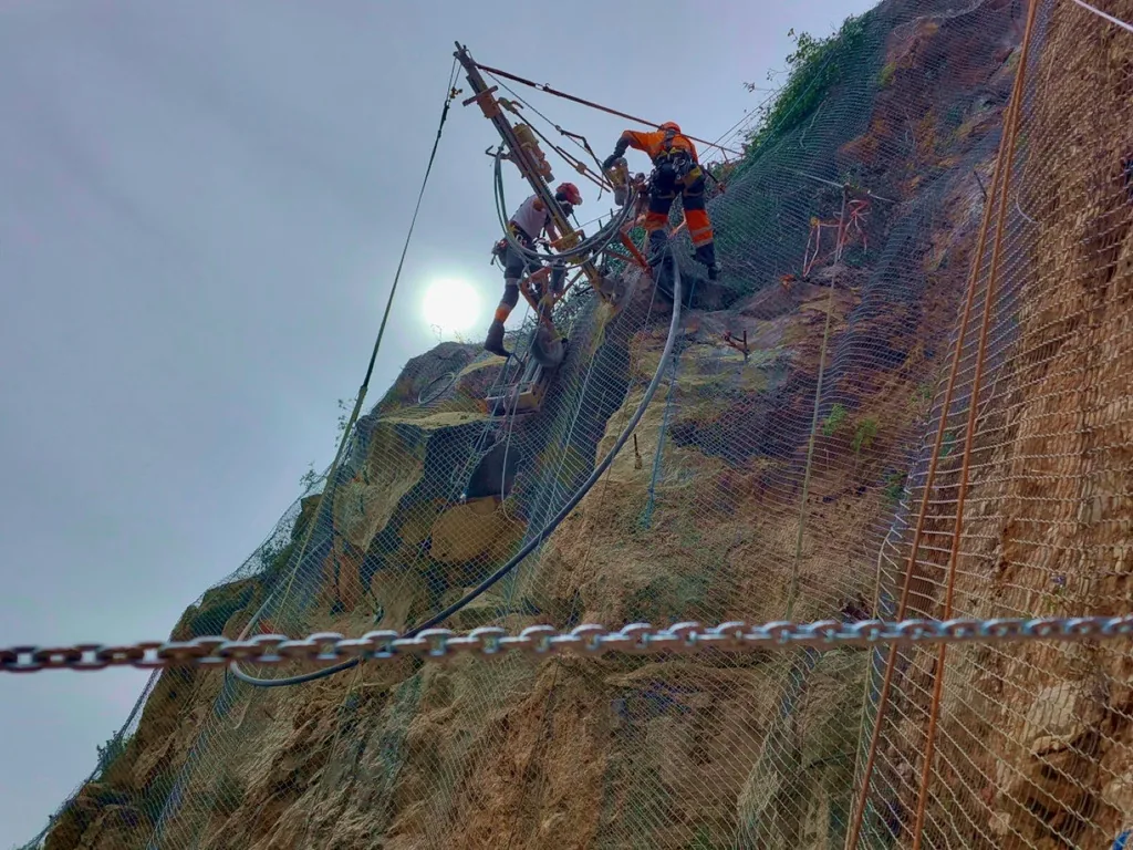 Rope access technicians drilling on a meshed embankment
