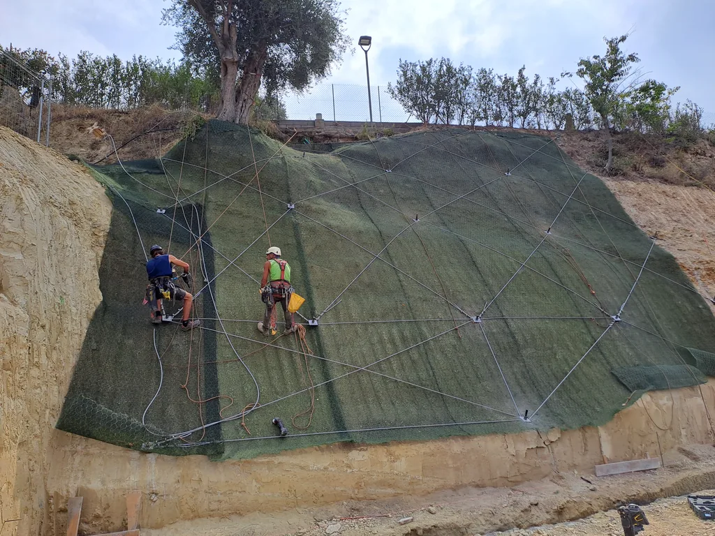 Two rope access technicians on an embankment covered with green geotextile