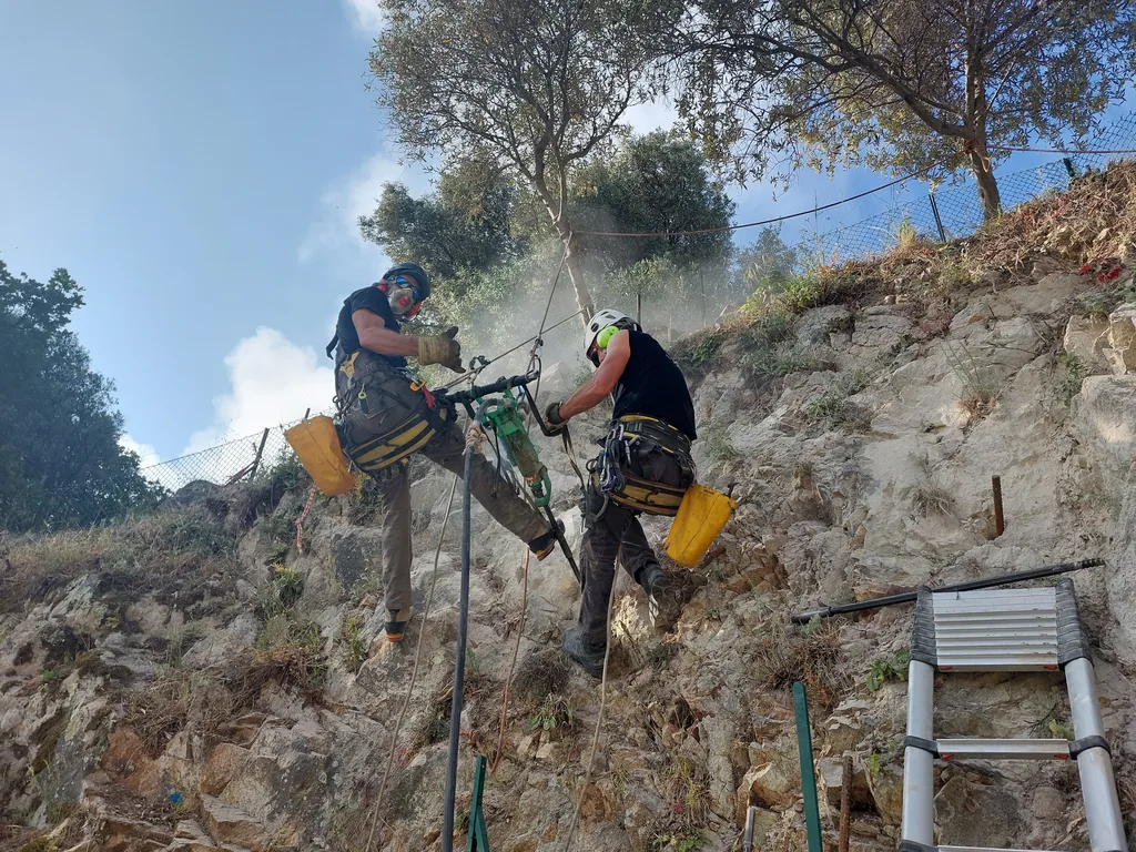 Two rope access technicians drilling on a rocky embankment