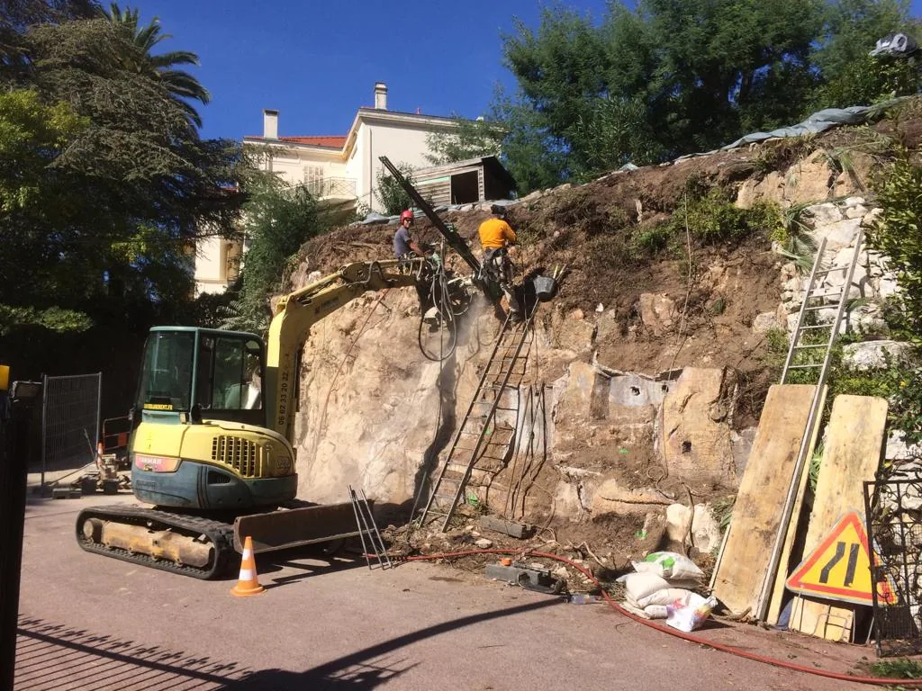 Excavator and rope access technicians drilling on a rock face