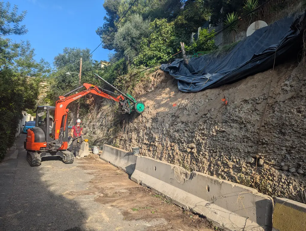 Mini excavator fitted with a drilling head on a roadside embankment